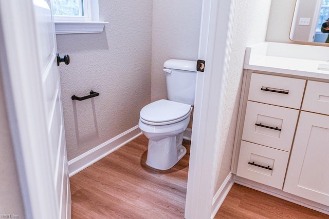 bathroom featuring baseboards, toilet, wood finished floors, a textured wall, and vanity