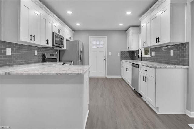 kitchen with light wood-style flooring, light stone countertops, white cabinets, and stainless steel appliances