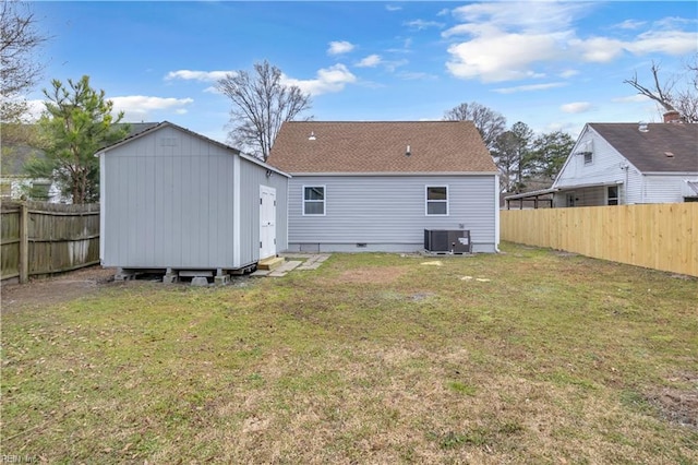 rear view of property featuring a lawn, cooling unit, an outdoor structure, and a fenced backyard