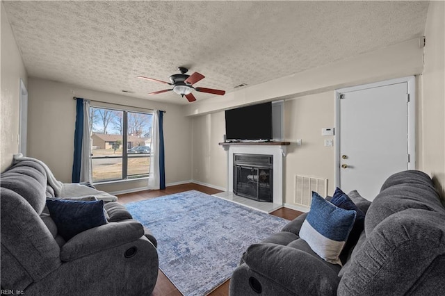 living area with a glass covered fireplace, wood finished floors, visible vents, and a textured ceiling