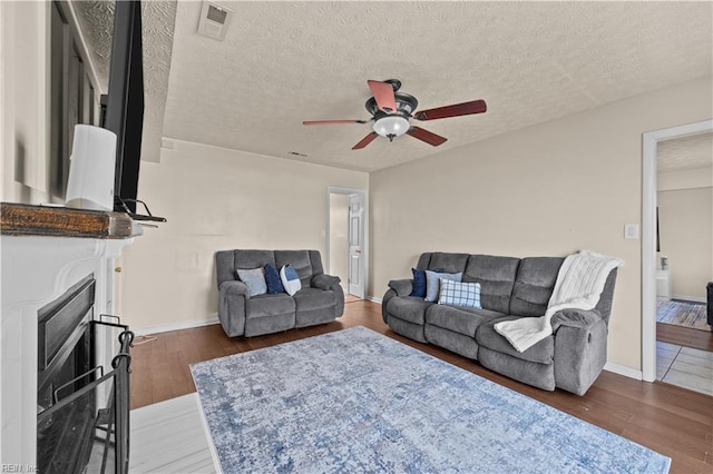 living area with a fireplace, wood finished floors, visible vents, and a textured ceiling