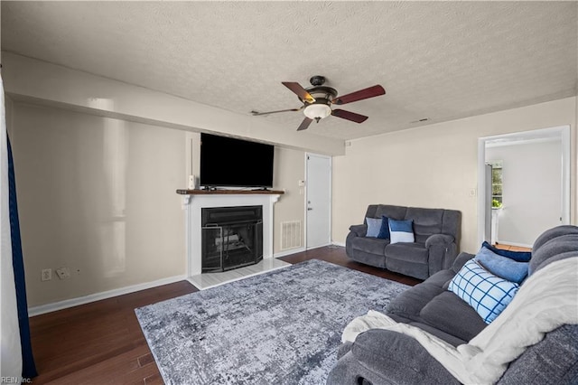 living room with baseboards, visible vents, dark wood finished floors, a fireplace with raised hearth, and a textured ceiling