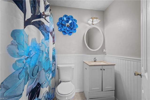 bathroom featuring vanity, a shower with shower curtain, toilet, and wainscoting