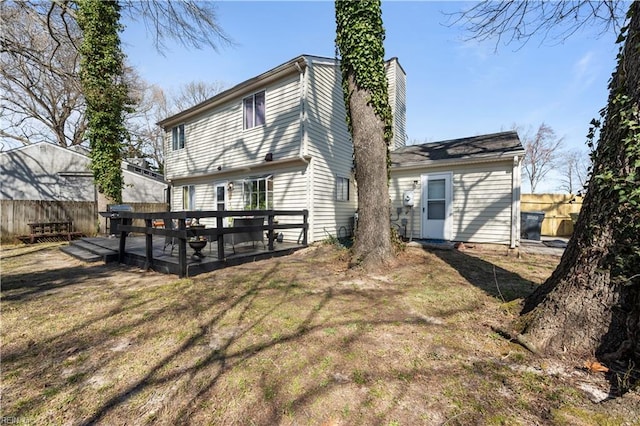 back of property with a deck, fence, a lawn, and a chimney