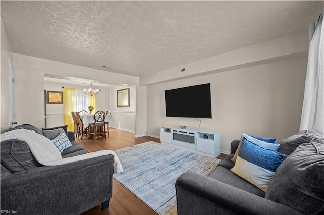 living room with a notable chandelier, visible vents, a textured ceiling, and wood finished floors