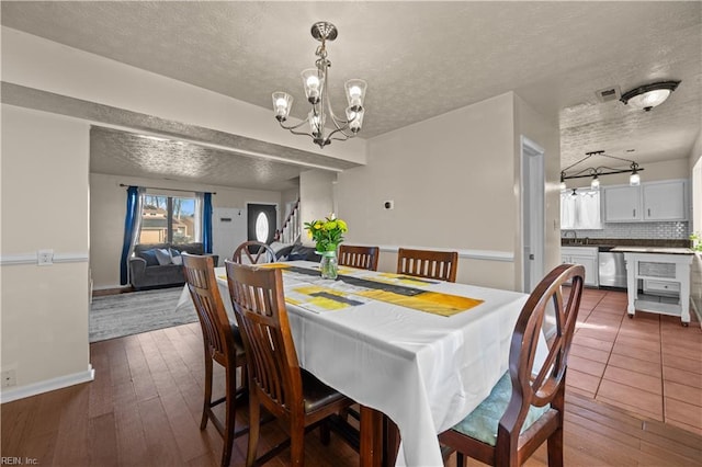 dining room with dark wood-style floors, baseboards, visible vents, a textured ceiling, and a notable chandelier