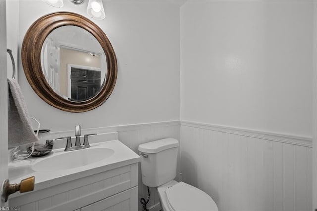 half bath with vanity, toilet, and wainscoting