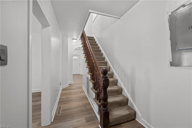 stairs with visible vents, wood finished floors, arched walkways, and baseboards