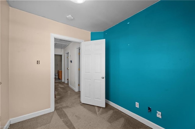 unfurnished bedroom featuring attic access, carpet flooring, and baseboards