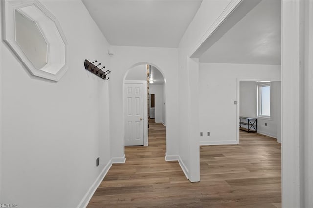 hallway featuring wood finished floors, arched walkways, and baseboards