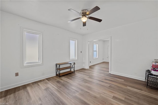 empty room with ceiling fan, visible vents, baseboards, and wood finished floors