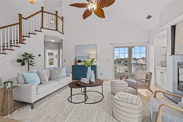 living area featuring a ceiling fan, visible vents, high vaulted ceiling, stairs, and light wood-type flooring