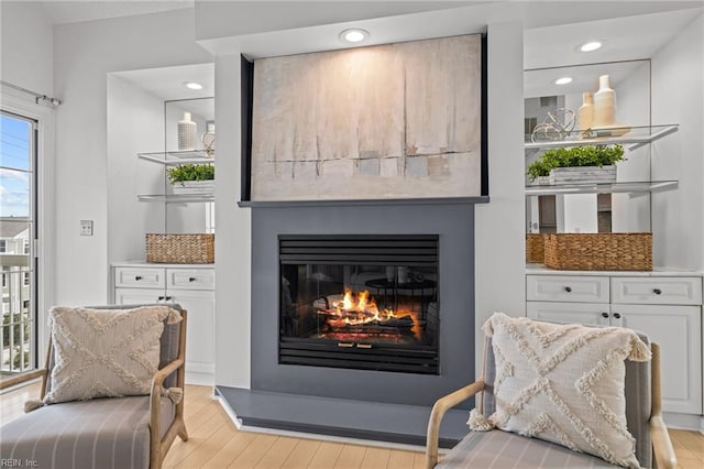 living area with a glass covered fireplace, light wood-style flooring, and recessed lighting