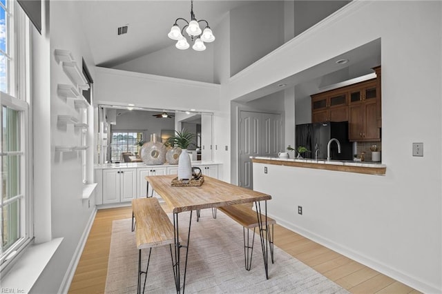 dining room with light wood finished floors, visible vents, high vaulted ceiling, and baseboards