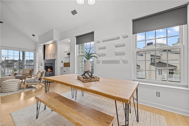 dining space with wood finished floors, baseboards, visible vents, high vaulted ceiling, and a lit fireplace