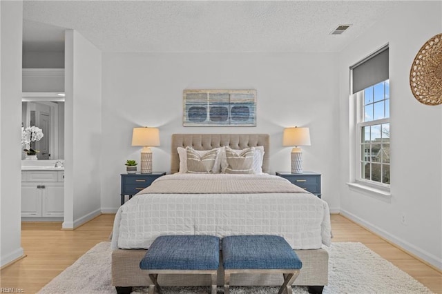 bedroom with visible vents, ensuite bathroom, a textured ceiling, light wood-style floors, and baseboards