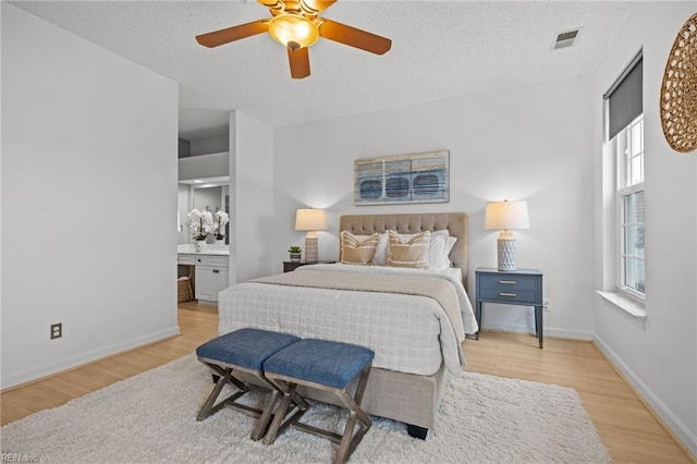 bedroom featuring visible vents, a textured ceiling, baseboards, and wood finished floors