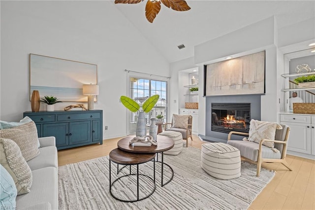 living room with a glass covered fireplace, visible vents, light wood-style floors, and ceiling fan