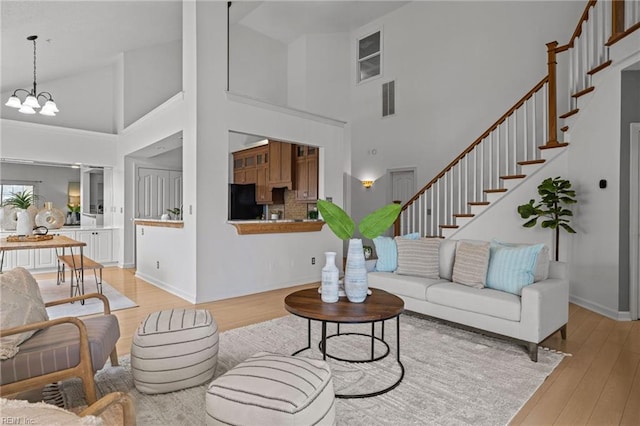 living area featuring visible vents, high vaulted ceiling, an inviting chandelier, stairs, and light wood-style floors