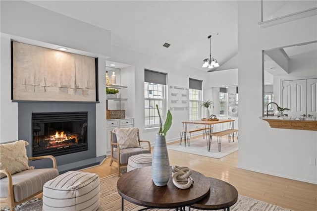 living area with a glass covered fireplace, an inviting chandelier, wood finished floors, and high vaulted ceiling