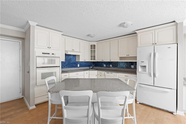 kitchen featuring light wood finished floors, tasteful backsplash, glass insert cabinets, a kitchen breakfast bar, and white appliances