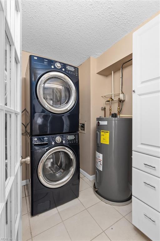 washroom featuring stacked washer and dryer, water heater, laundry area, light tile patterned flooring, and a textured ceiling
