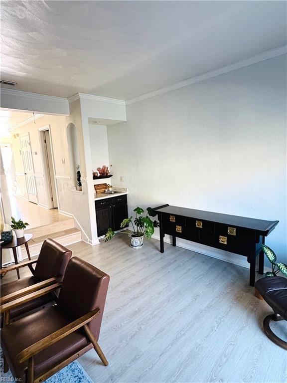 living area featuring visible vents, light wood-style flooring, baseboards, and ornamental molding