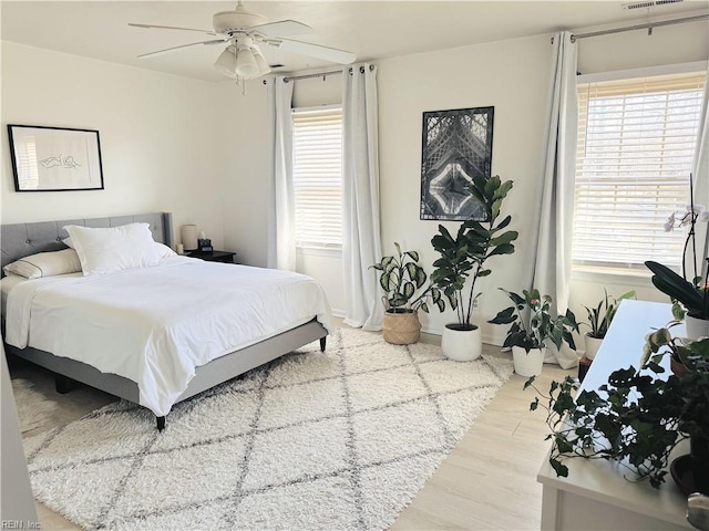 bedroom with ceiling fan, visible vents, multiple windows, and wood finished floors