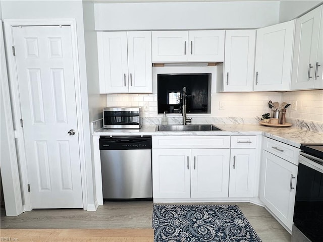 kitchen featuring a sink, backsplash, white cabinetry, stainless steel appliances, and light wood finished floors