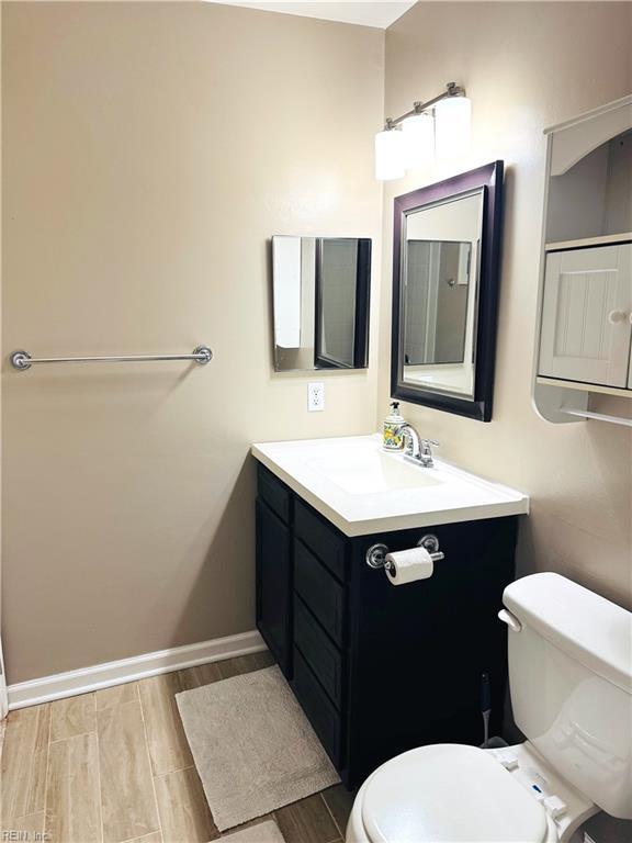 half bathroom featuring wood finish floors, baseboards, toilet, and vanity