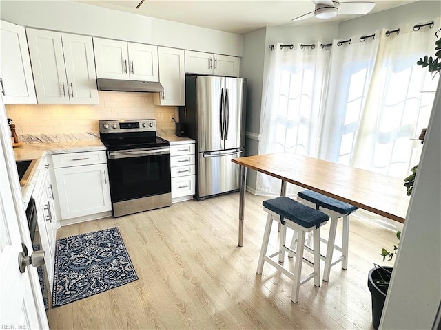 kitchen featuring light wood-style flooring, light countertops, under cabinet range hood, appliances with stainless steel finishes, and backsplash