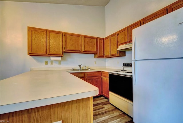 kitchen with under cabinet range hood, light countertops, brown cabinets, white appliances, and a sink