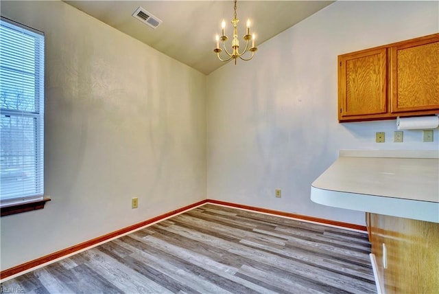 unfurnished dining area featuring visible vents, baseboards, an inviting chandelier, and wood finished floors