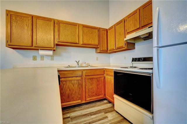 kitchen featuring white appliances, brown cabinetry, a sink, light countertops, and under cabinet range hood