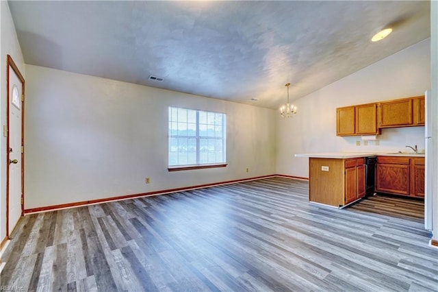 kitchen with brown cabinetry, visible vents, wood finished floors, a peninsula, and a notable chandelier