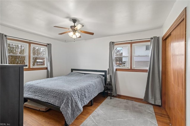 bedroom with a closet, baseboards, wood finished floors, and a ceiling fan