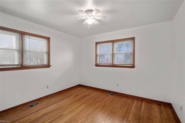 spare room with light wood-type flooring, visible vents, baseboards, and a ceiling fan