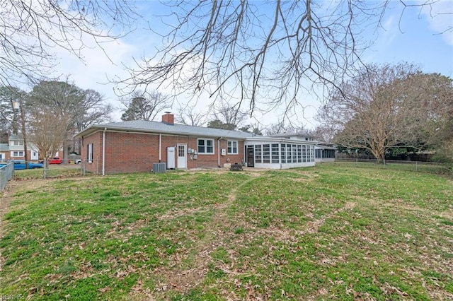 rear view of property featuring a yard, a fenced backyard, a sunroom, a chimney, and brick siding