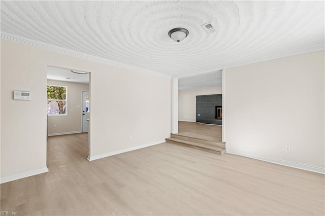 unfurnished room with baseboards, visible vents, light wood finished floors, and a lit fireplace