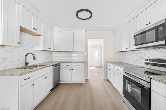 kitchen with light stone countertops, a sink, white cabinets, appliances with stainless steel finishes, and light wood-type flooring