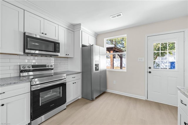 kitchen with light wood finished floors, visible vents, decorative backsplash, white cabinets, and stainless steel appliances