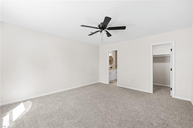 unfurnished bedroom with a walk in closet, baseboards, light colored carpet, a closet, and ensuite bath