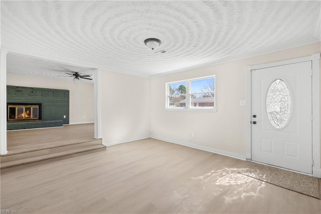 foyer with a fireplace, wood finished floors, a ceiling fan, and baseboards