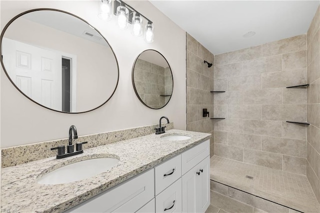 bathroom with double vanity, a tile shower, and a sink