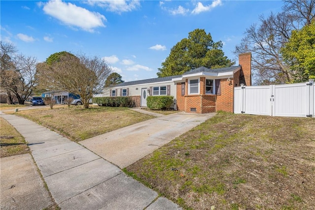 ranch-style home featuring brick siding, a front lawn, a chimney, driveway, and a gate