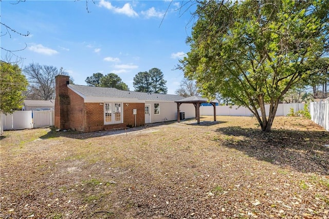 exterior space with a fenced backyard, a gazebo, french doors, brick siding, and a chimney