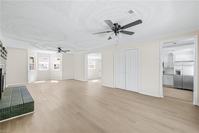 unfurnished living room featuring visible vents, light wood-style flooring, a fireplace, and ceiling fan