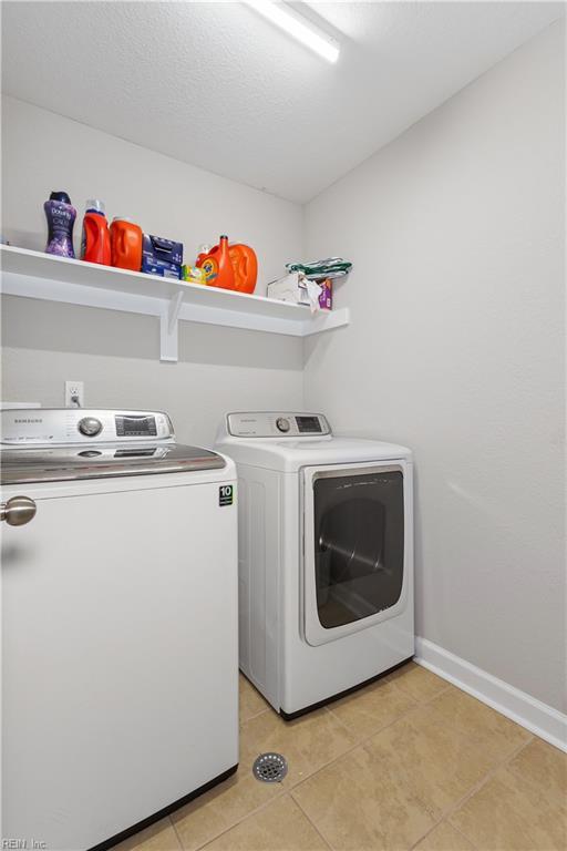 laundry area with a textured ceiling, separate washer and dryer, light tile patterned floors, baseboards, and laundry area