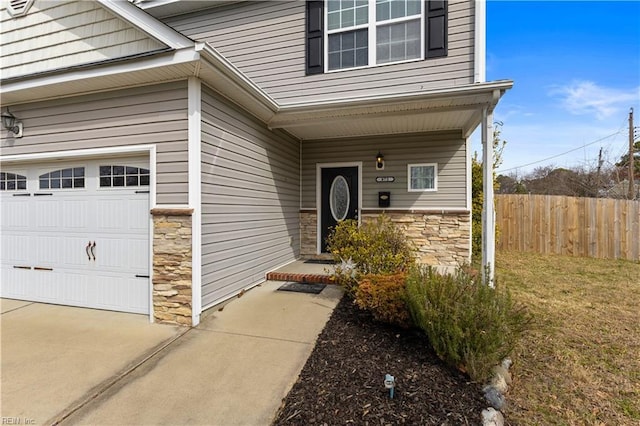 doorway to property featuring stone siding, driveway, and fence