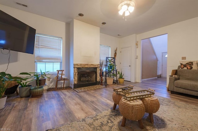 living area featuring a fireplace, wood finished floors, visible vents, and a ceiling fan